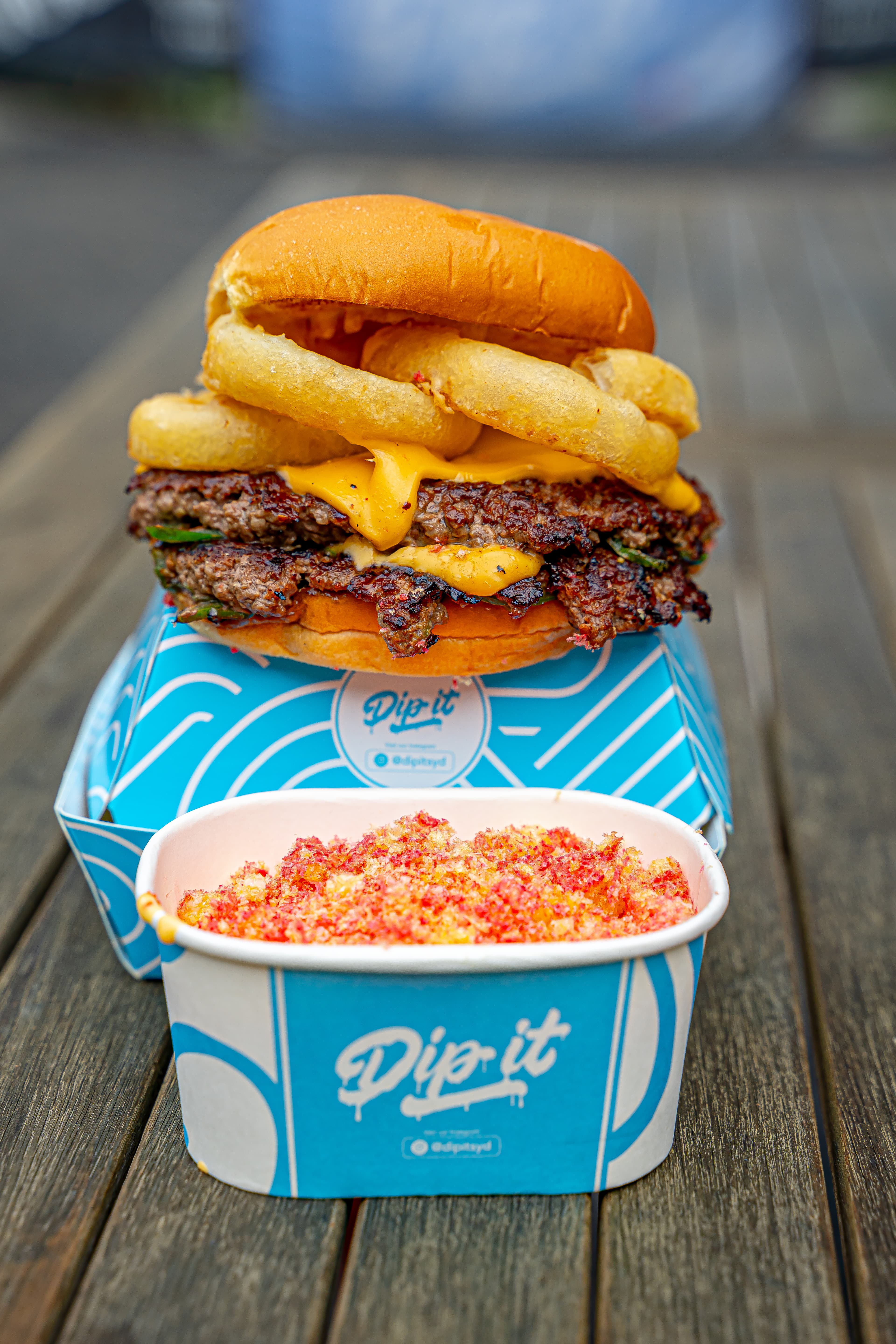 Flamin' Hot Fozball burger on wooden table with Dip It queso dip cup